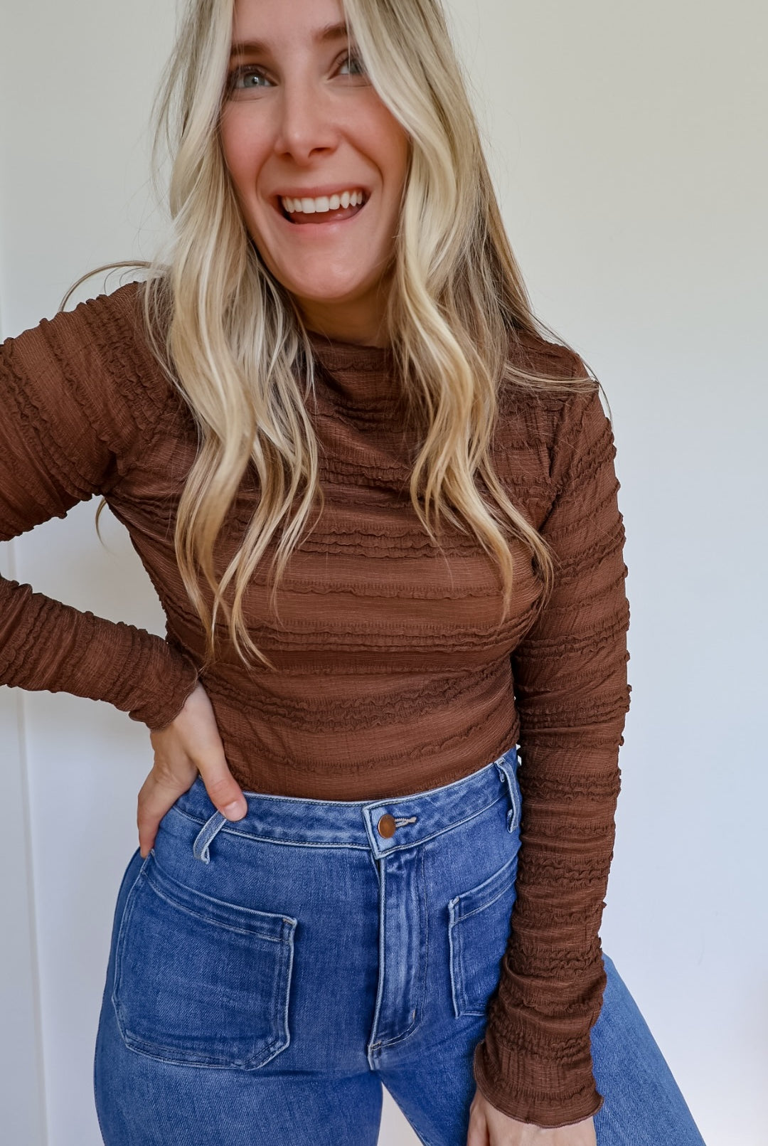 Woman wearing a brown shirred long sleeve mock neck top with blue jeans.