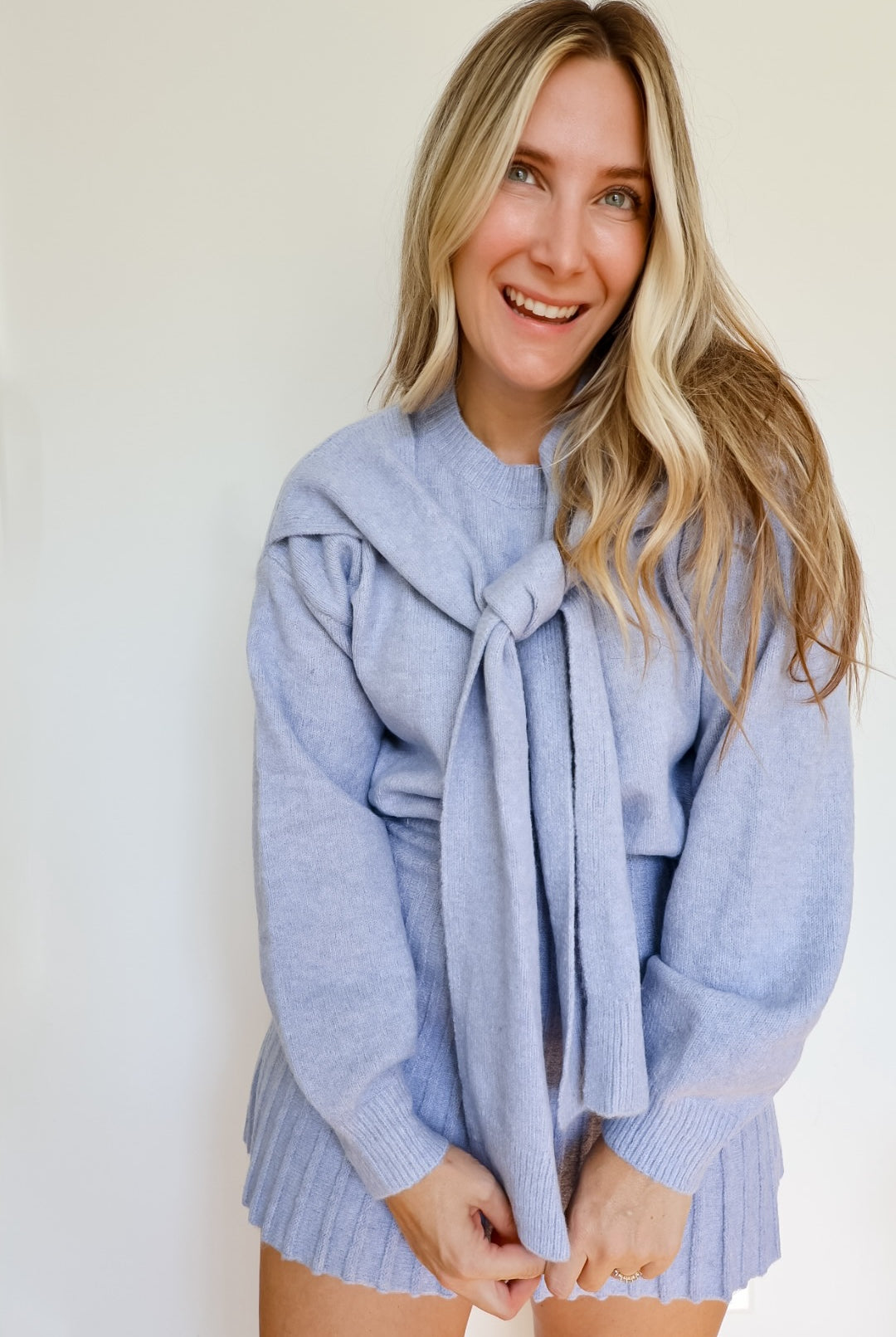 Woman wearing a sky blue knit sweater and pleated skirt set with a tie around the neck.