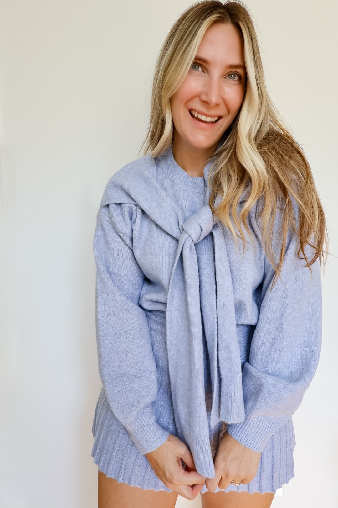 Woman wearing a sky blue knit sweater and pleated skirt set with a tie around the neck.