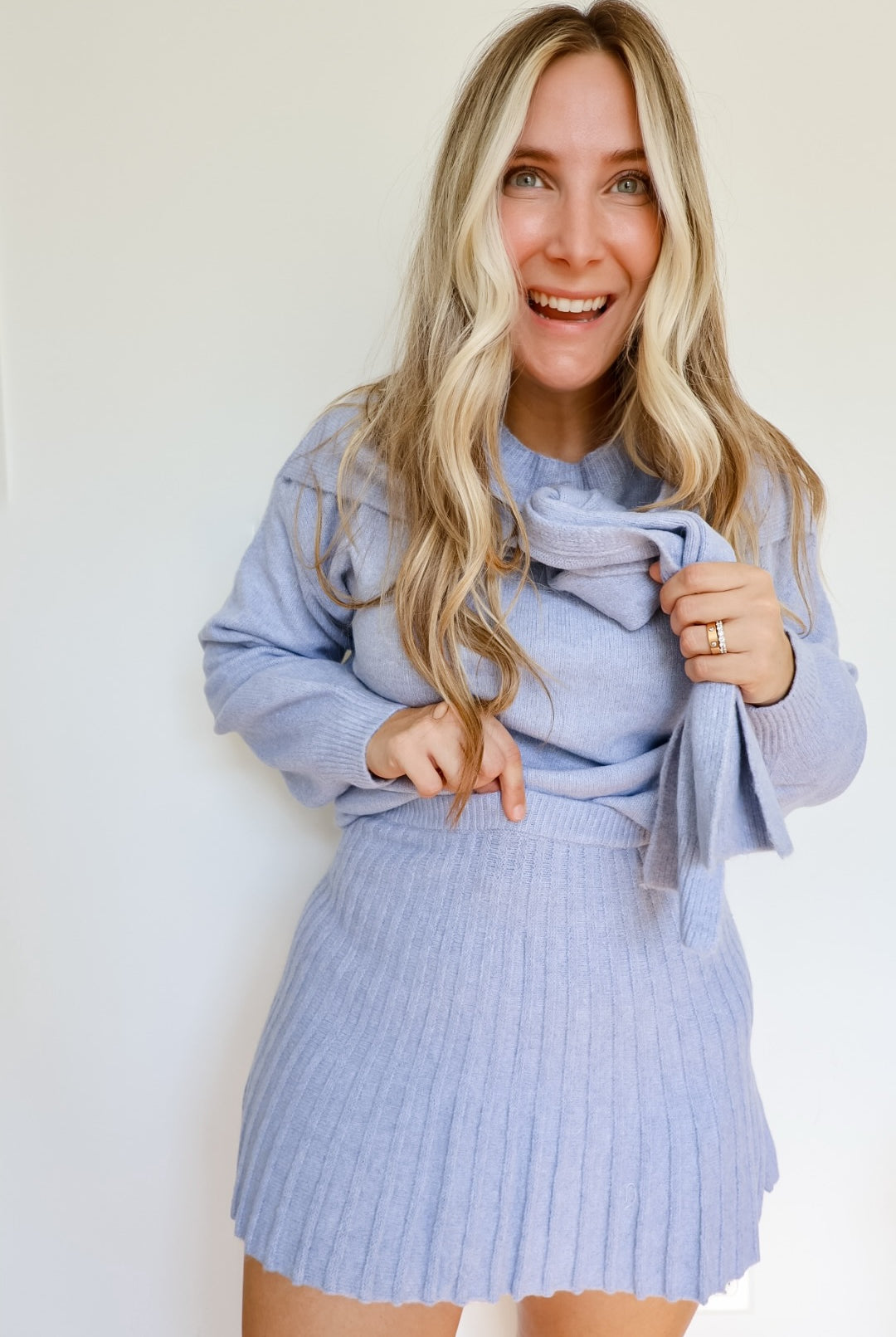 Woman wearing a sky blue knit sweater and pleated skirt set with a tie around the neck.