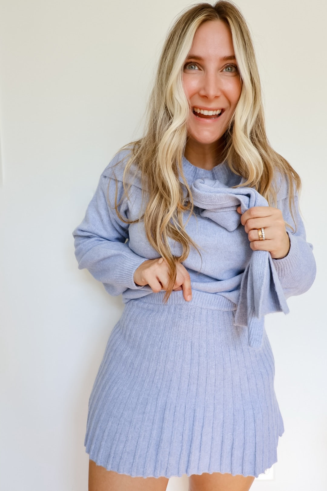 Woman wearing a sky blue knit sweater and pleated skirt set with a tie around the neck.