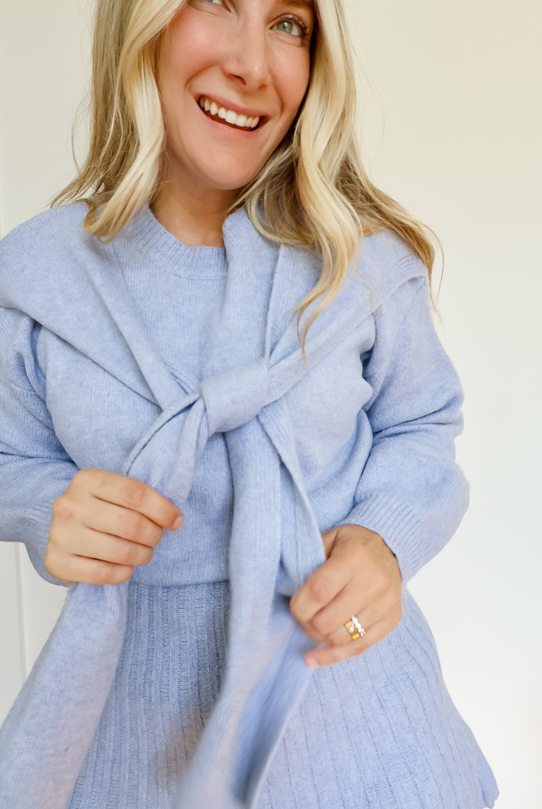 Woman wearing a sky blue knit sweater and pleated skirt set with a tie around the neck.