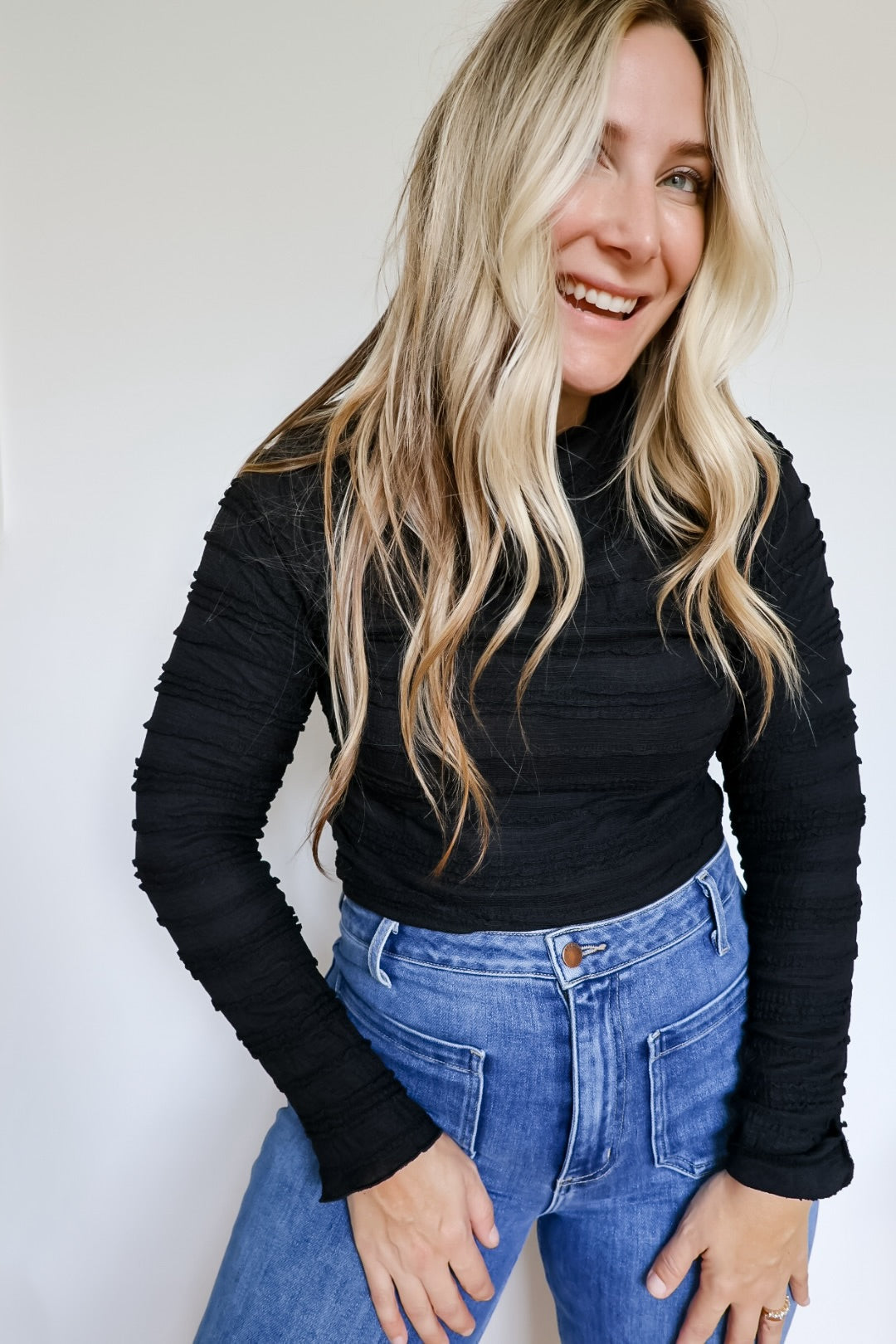 Woman wearing a black shirred long sleeve mock neck top paired with blue jeans.