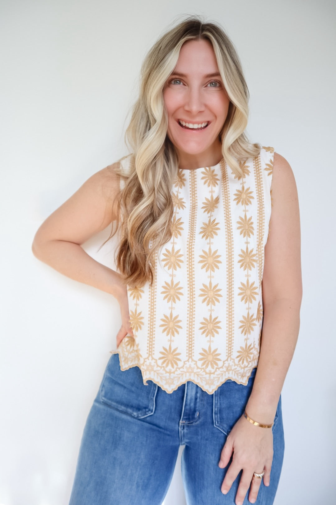 Woman wearing a sleeveless top with a geometric pattern and blue jeans against a white background