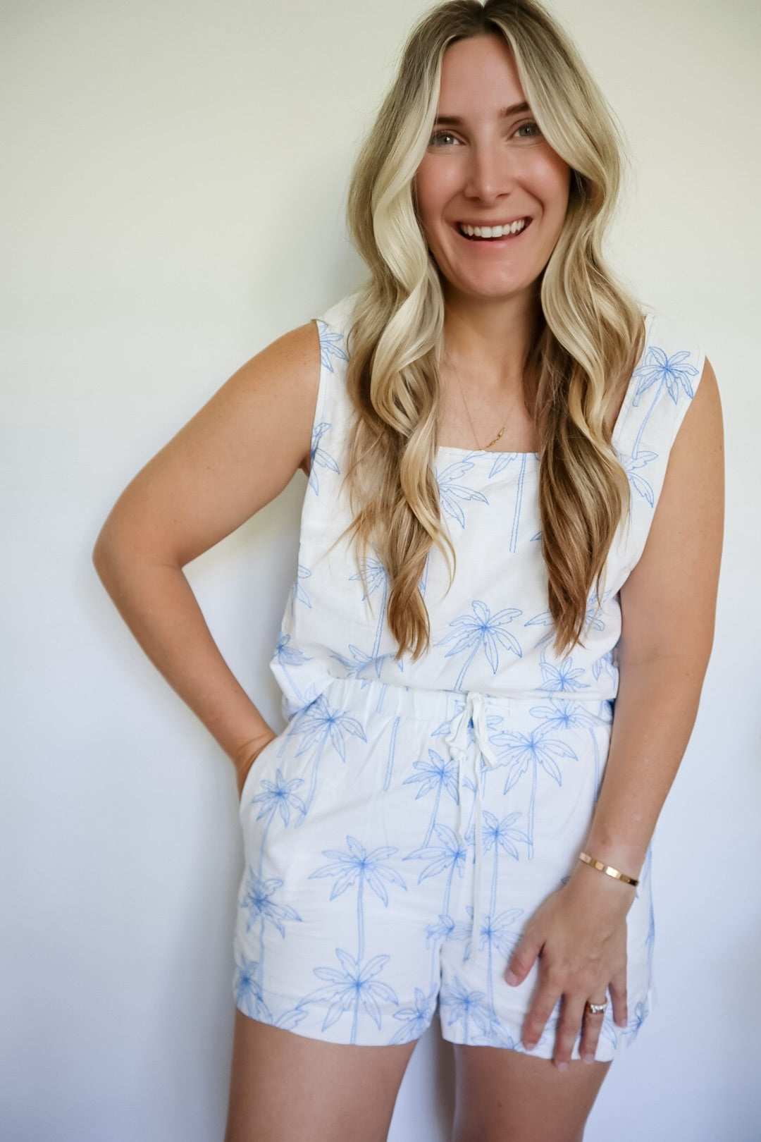 Woman wearing a white set with blue floral pattern against a plain background