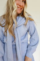 Woman wearing a sky blue knit sweater and pleated skirt set with a tie around the neck.
