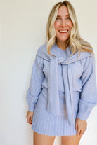 Woman wearing a sky blue knit sweater and pleated skirt set with a tie around the neck.