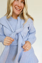 Woman wearing a sky blue knit sweater and pleated skirt set with a tie around the neck.